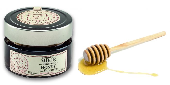 Leonardi honey condiment in a glass jar beside honey and a wooden dipper